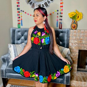 May include: A black halter dress with colorful floral embroidery. The dress has a fitted bodice and a flowing skirt. The embroidery features red, orange, yellow, green, blue, and purple flowers.