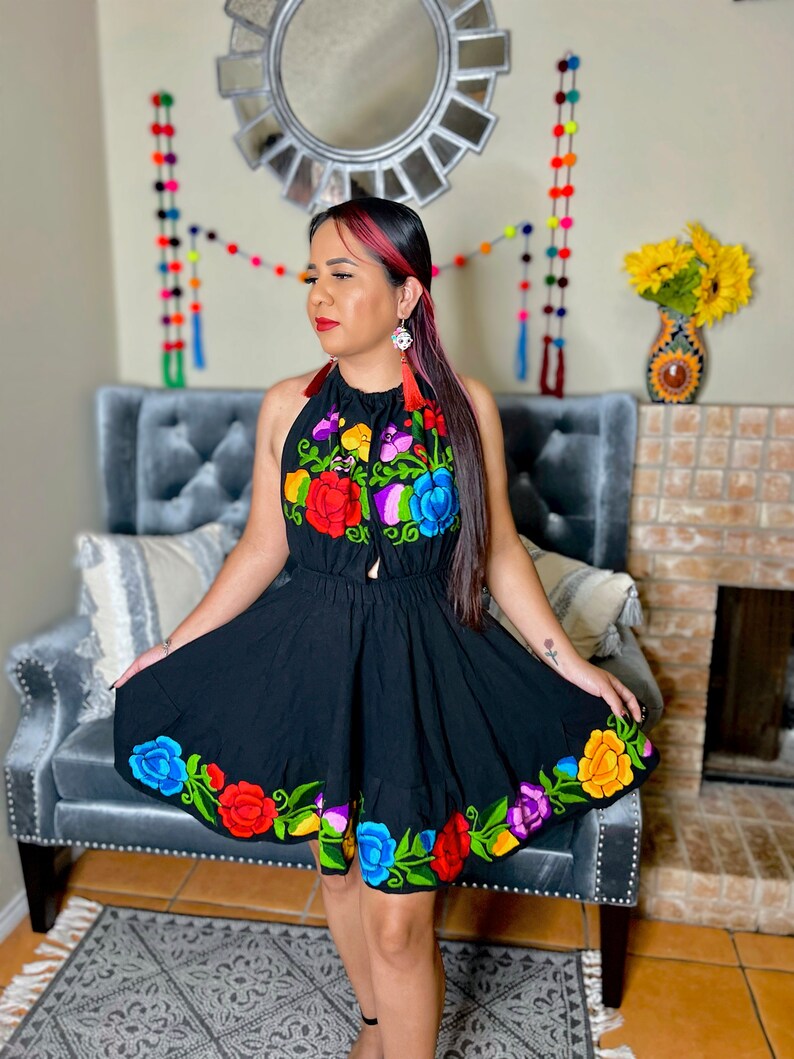 May include: A black halter dress with colorful floral embroidery. The dress has a fitted bodice and a flowing skirt. The embroidery features red, orange, yellow, green, blue, and purple flowers.