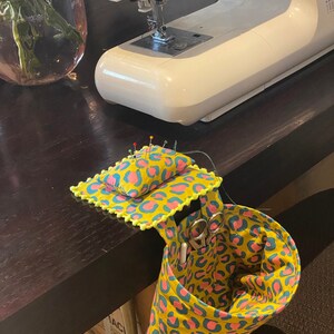 May include: A yellow and pink leopard print fabric sewing organizer with a pincushion and a pocket for scissors and other sewing tools.