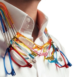 Puede incluir: Un conjunto de seis gafas de lectura coloridas con brazos flexibles, colgadas alrededor del cuello de una persona. Las gafas son de varios colores, incluyendo rojo, azul, verde, amarillo, rosa y naranja.