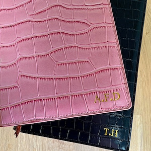 May include: Two leather journals with embossed crocodile patterns. The top journal is pink with the initials "A.F.D." embossed in gold. The bottom journal is black with the initials "T.H." embossed in gold.