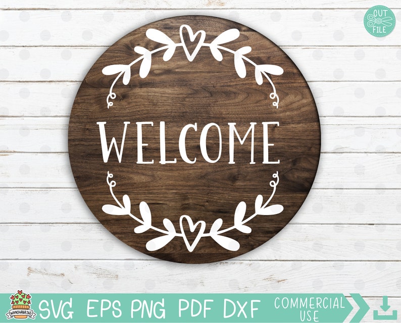 May include: A round wooden sign with the word "WELCOME" in white lettering. The sign is decorated with a white wreath of leaves and hearts.