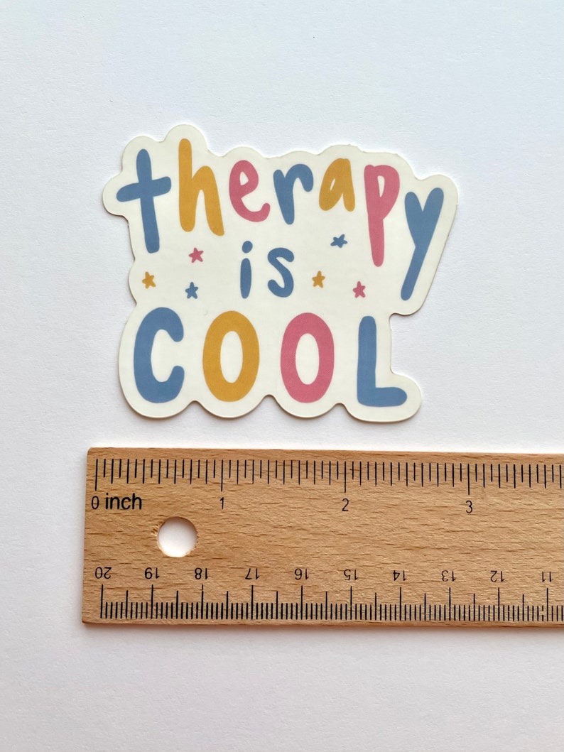 May include: A sticker with the text "therapy is cool" in blue, yellow, and pink lettering with small pink stars. The sticker is about 2 inches wide.