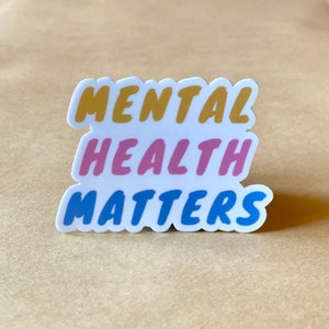 May include: A white sticker with the text "MENTAL HEALTH MATTERS" in bold, colorful letters. The words "MENTAL" are in yellow, "HEALTH" are in pink, and "MATTERS" are in blue.