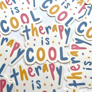 May include: Multiple stickers with the text "therapy is cool" in blue, yellow, pink, and white lettering with small white stars on a white background.
