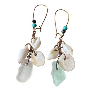 Peut inclure: Une paire de boucles d'oreilles créoles dorées avec un accent de perle turquoise et noire. Chaque boucle d'oreille présente un groupe de coquillages blancs et un charme en verre de mer vert clair.
