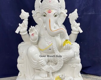 May include: White marble statue of Ganesha, the Hindu god of wisdom and prosperity, sitting on a throne with a mouse at his feet. The statue is decorated with intricate details and has a yellow and gold paint finish. The statue is labeled "Gour Moorti Kala".