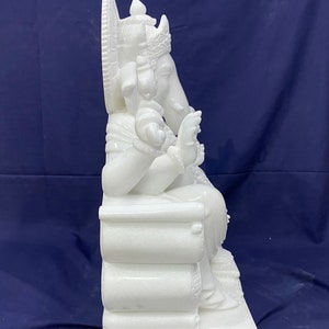Op de afbeelding: Wit marmeren beeld van Ganesha, de hindoe&iuml;stische god van wijsheid en voorspoed, zittend op een troon. Het beeld is ingewikkeld gebeeldhouwd met details op de troon en Ganesha's kleding.
