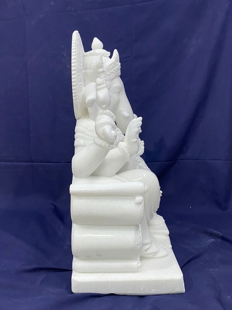 Op de afbeelding: Wit marmeren beeld van Ganesha, de hindoe&iuml;stische god van wijsheid en voorspoed, zittend op een troon. Het beeld is ingewikkeld gebeeldhouwd met details op de troon en Ganesha's kleding.