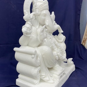 Op de afbeelding: Wit marmeren beeld van Ganesha, de hindoe&iuml;stische god van wijsheid en voorspoed, zittend op een troon met zijn slurf omhoog en een snoepje in zijn hand.