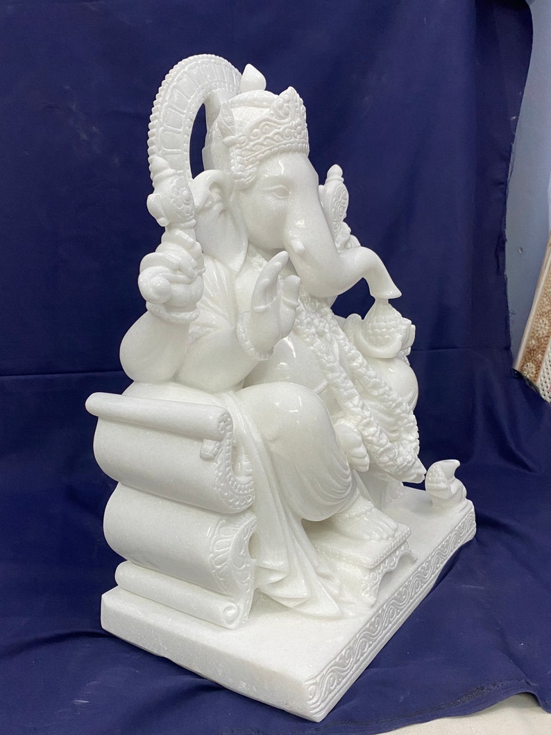 Op de afbeelding: Wit marmeren beeld van Ganesha, de hindoe&iuml;stische god van wijsheid en voorspoed, zittend op een troon met zijn slurf omhoog en een snoepje in zijn hand.