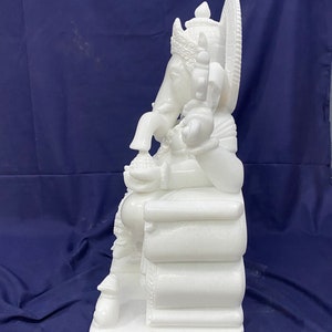 Op de afbeelding: Wit marmeren beeld van Ganesha, de hindoe&iuml;stische god van wijsheid en voorspoed, zittend op een troon. Het beeld is ingewikkeld gedetailleerd en heeft een kroon, een slurf en een grote buik.