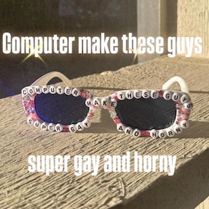 Może przedstawiać: Okulary przeciwsłoneczne z białą oprawką i ciemnymi soczewkami, ozdobione tekstem z koralików. Tekst na okularach brzmi "COMPUTER SUPER GAY MAKE THESE GUYS AND HORNY". Dodatkowy tekst na dole mówi "super gay and horny".