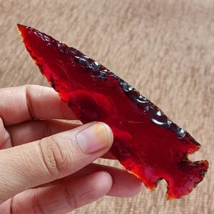 May include: A deep red arrowhead with a translucent, almost glassy appearance. The arrowhead is pointed and has a sharp edge.