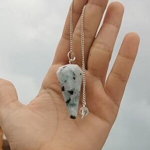 Può includere: Un pendolo di cristallo bianco e nero su una catena d'argento. Il pendolo ha la forma di una lacrima e ha una sfera di cristallo trasparente alla fine della catena.