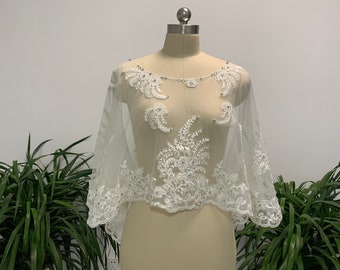 May include: A white lace bridal shrug with a beaded design. The shrug has a scoop neckline and three-quarter sleeves.