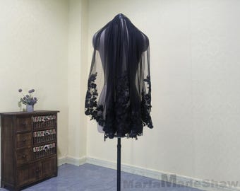 May include: A black lace wedding veil with a scalloped edge. The veil is on a mannequin and is displayed against a white wall.