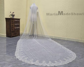 May include: A long, white bridal veil with a beaded lace trim. The veil is draped over a dress form and is shown from the back.