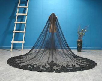 May include: A black bridal veil with intricate lace detailing along the hem. The veil is displayed on a mannequin against a blue backdrop. A wooden ladder and a decorative vase are also visible.