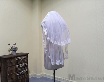 May include: A white bridal veil with a single layer of lace trim. The veil is displayed on a mannequin.