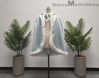 May include: A light blue hooded cape with a white faux fur trim. The cape is on a mannequin and has a white satin bow at the neck.