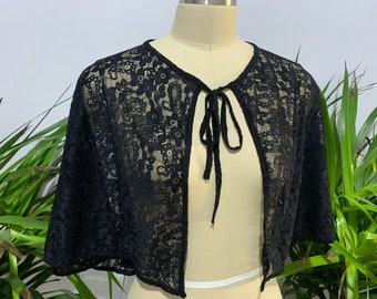 Könnte beinhalten: Schwarze Spitzenjacke mit einem Bindeverschluss am Hals. Die Jacke ist durchsichtig und zart und eignet sich perfekt zum Überziehen über ein Kleid oder ein Oberteil.