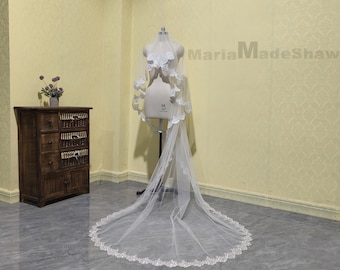 May include: A white bridal veil with a delicate lace trim. The veil is displayed on a mannequin and is flowing on the floor. The text "MariaMadeShawls" is visible in the background.