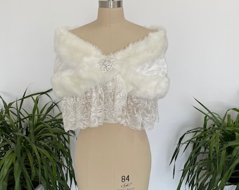 May include: White faux fur shawl with a lace trim and a rhinestone brooch. The shawl is draped over a dress form.