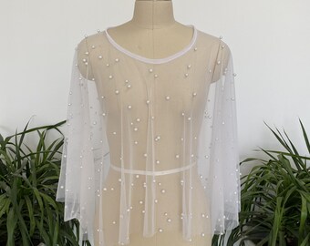 May include: White sheer mesh cape with pearl embellishments. The cape has a round neckline and long sleeves.