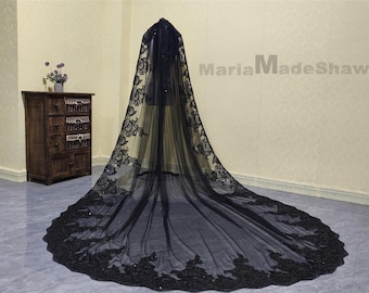 May include: A black tulle wedding veil with a lace trim. The veil is long and flowing, and the lace trim is intricate and detailed.