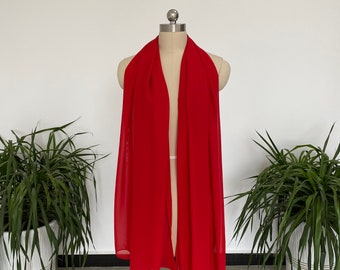 May include: A red sheer scarf draped over a mannequin. The scarf is made of a lightweight fabric and has a flowing drape.