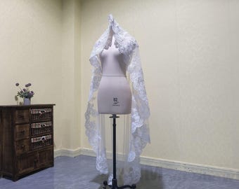 May include: A white bridal veil with delicate lace detailing. The veil is displayed on a mannequin and is long and flowing.
