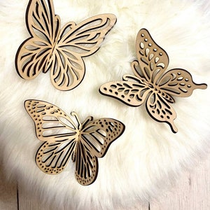 May include: Three wooden butterfly wall decor pieces in a light brown color. The butterflies are intricately cut with a delicate design and have a natural wood finish.