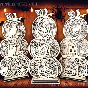 May include: Three-tiered wooden Halloween pumpkin decorations with intricate cut-out designs. Each pumpkin features a different spooky theme, including a raven, cat, skull, and haunted house. The pumpkins are white and stand on a wooden surface.
