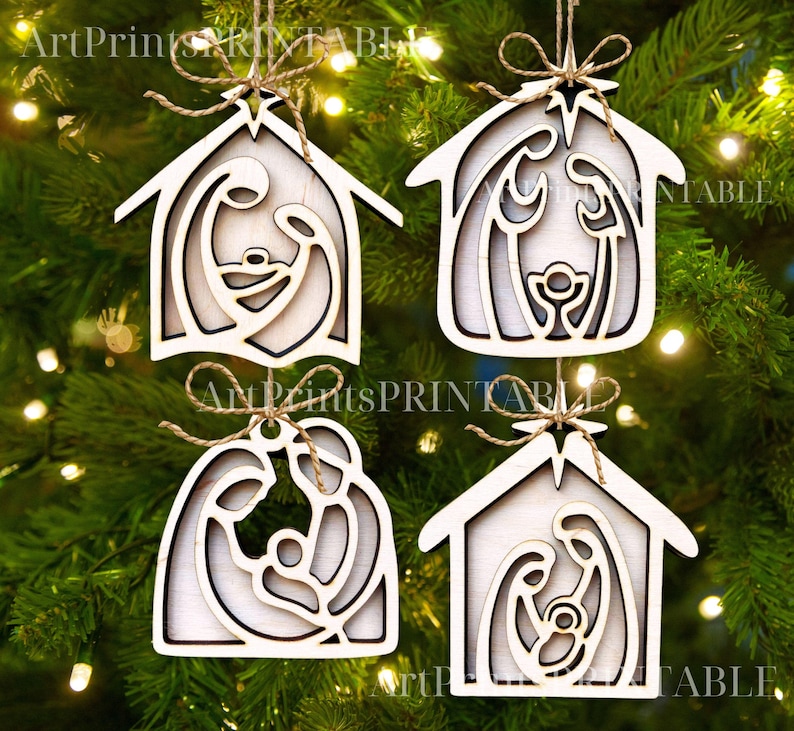May include: Four wooden Christmas ornaments in the shape of a house, each featuring a layered Nativity scene. The ornaments are light-colored with a natural wood grain, and are suspended by twine. The ornaments are hanging on a green Christmas tree.