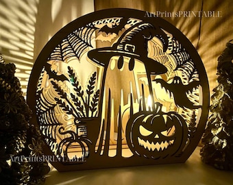May include: Wooden Halloween-themed decorative light with a circular frame. The design features a ghost wearing a witch hat, a jack-o'-lantern, bats, and spiderwebs. The text "ArtPrintsPRINTABLE" is visible.