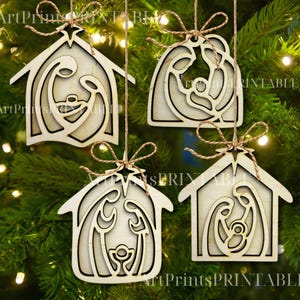 May include: Four wooden Christmas ornaments depicting the Nativity scene, hanging from twine. Each ornament is a light-colored wooden cutout of a house shape or a curved shape, with the Nativity figures inside. The ornaments are hanging on a Christmas tree.