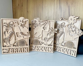 May include: Three wooden plaques with laser-cut designs of golfers and golf bags. The plaques are labeled "Brain", "Kevin", and "Kevin".