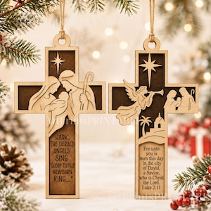 May include: Two light-colored wooden cross ornaments featuring dark brown cutouts. The left cross depicts the Nativity scene with text reading, "Hark, the herald angels sing, glory to the newborn king." The right cross shows an angel and the Nativity with text from Luke 2:11.