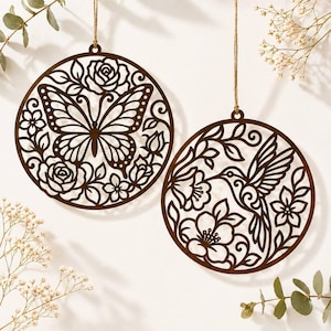 May include: Two brown, circular wooden ornaments with intricate cut-out designs. One features a butterfly surrounded by flowers, the other a hummingbird and blossoms. Both are suspended by twine, perfect for home decor.