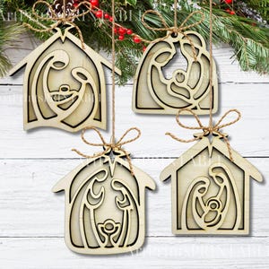 May include: Four wooden Christmas ornaments with a nativity scene design. Each ornament is shaped like a house and features a laser-cut depiction of Mary, Joseph, and baby Jesus. They are tied with twine and hang from a Christmas tree.