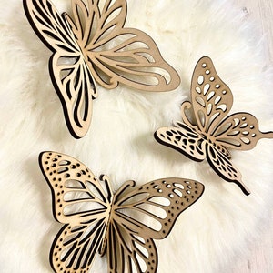 May include: Three wooden butterfly wall decor pieces in a light brown color. The butterflies are intricately cut with a delicate design and have a distressed finish.