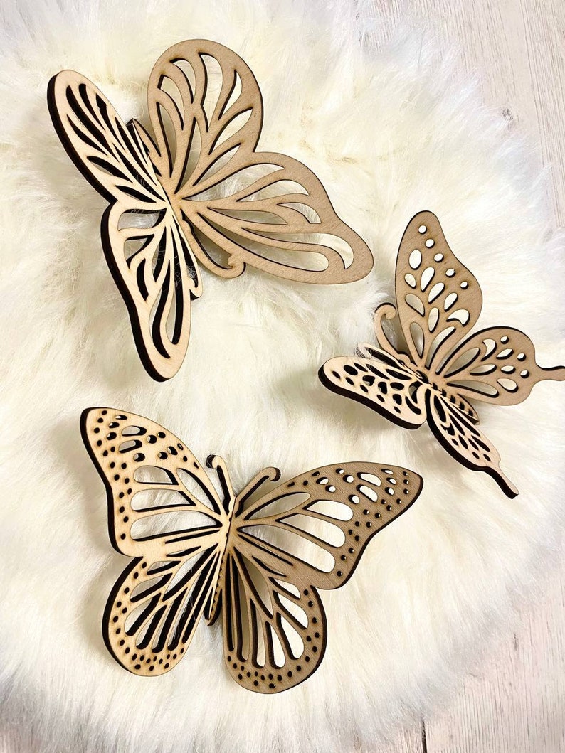 May include: Three wooden butterfly wall decor pieces in a light brown color. The butterflies are intricately cut with a delicate design and have a distressed finish.