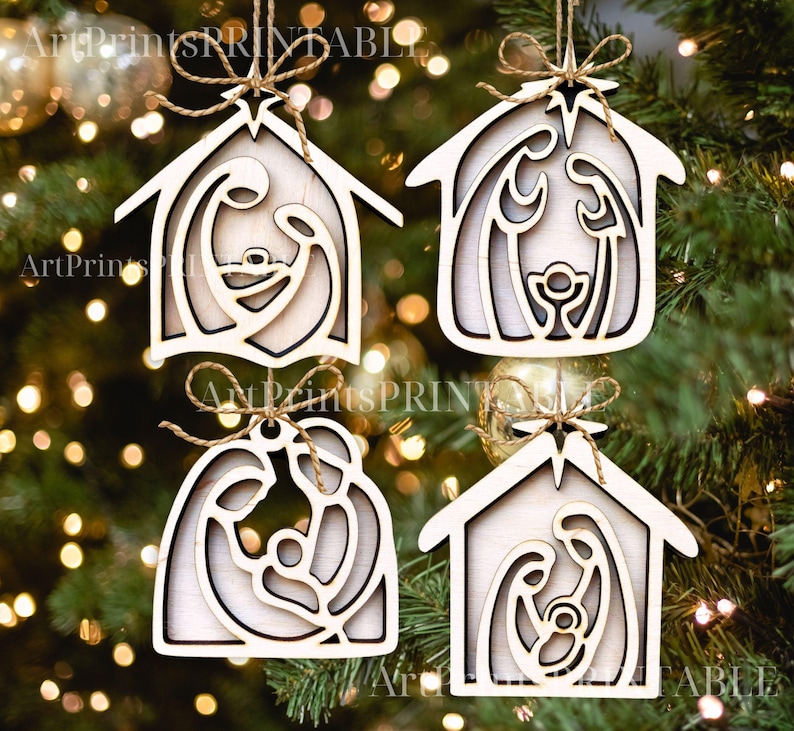 May include: Four wooden Christmas ornaments in the shape of a house, each featuring a nativity scene cutout. The ornaments are light-colored with a natural wood grain, and are suspended by twine. The background is a blurred Christmas tree.