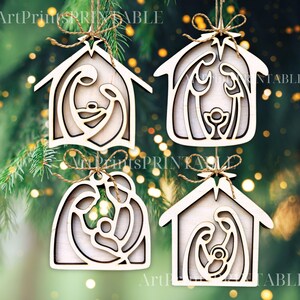 May include: Four wooden Christmas ornaments in the shape of a house, each featuring a Nativity scene. The ornaments are light brown with a natural wood grain, and are suspended by twine. The background is a blurred green with bokeh lights.