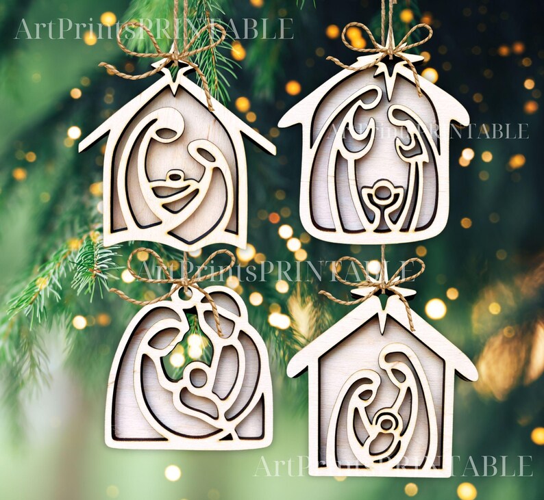 May include: Four wooden Christmas ornaments in the shape of a house, each featuring a Nativity scene. The ornaments are light brown with a natural wood grain, and are suspended by twine. The background is a blurred green with bokeh lights.