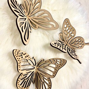 May include: Three wooden butterfly wall decor pieces in various sizes and designs. The butterflies are made of light brown wood and have intricate cutouts.