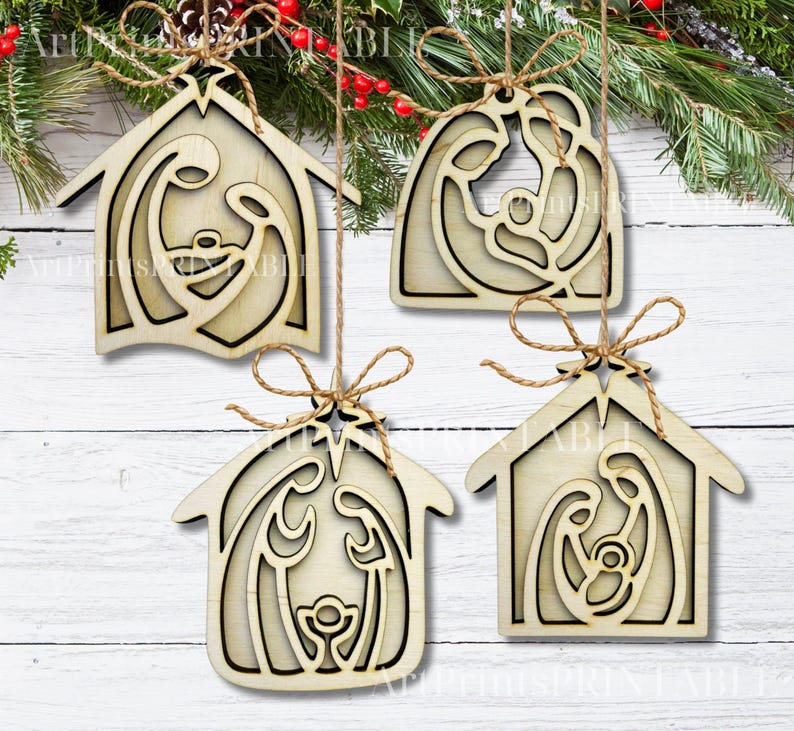 May include: Four wooden Christmas ornaments with a nativity scene design. Each ornament is shaped like a house and features a laser-cut depiction of Mary, Joseph, and baby Jesus. They are tied with twine and hang from a Christmas tree.