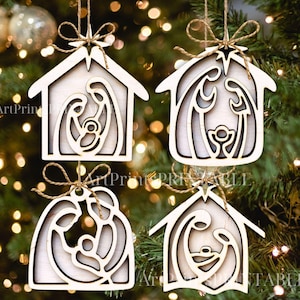 May include: Four wooden Christmas ornaments with a nativity scene design. Each ornament is a house shape with a cutout of Mary, Joseph, and baby Jesus. They are strung with twine and have a star at the top.