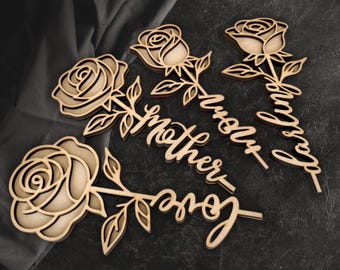 May include: Wooden laser-cut roses with the words "love", "mother", and "family". The roses are light brown with detailed petals and leaves. The background is a dark gray surface.